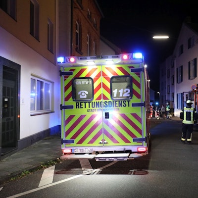 Ein Einsatzwagen des Rettungsdienstes steht nachts in einer Wohnstraße, im Hintergrund sind auch ein Fahrzeug der Feuerwehr und Feuerwehrleute zu sehen.