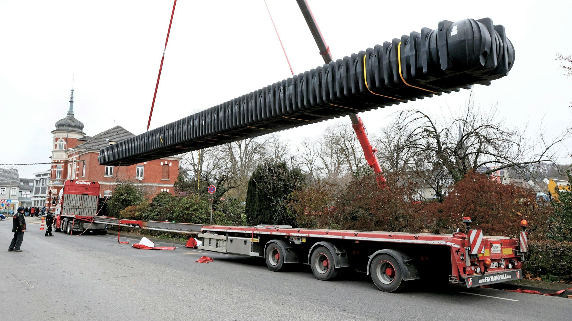 Der 30 Meter lange Regenwassertank wird am Haken eines Autokrans vom Lkw an der Neukirchener Straße in die Baugrube im Leichlinger Stadtpark gehoben.