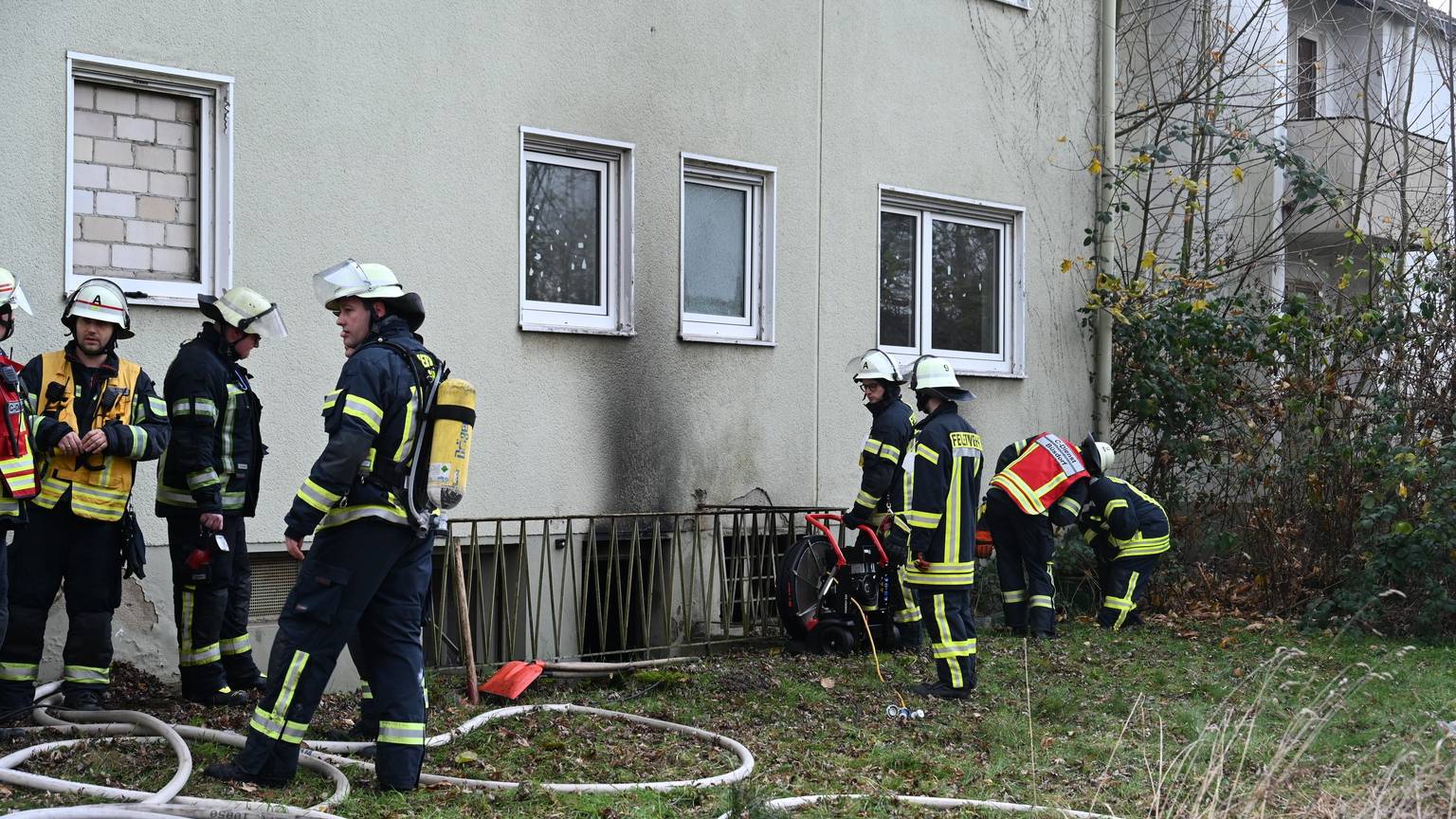 Feuerwehrleute stehen vor der rußgeschwärzten Fassade eines Hauses in Bergheim.