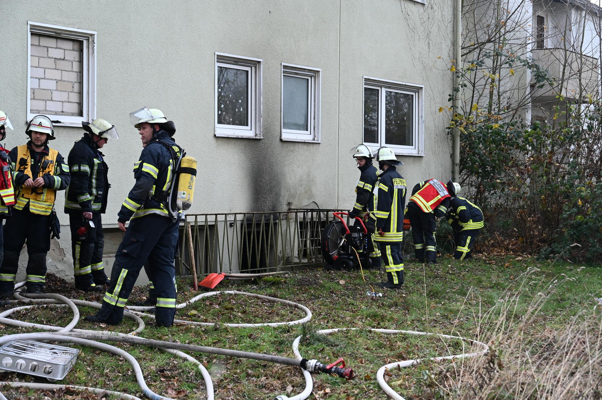 Feuerwehrleute stehen vor der rußgeschwärzten Fassade eines Hauses in Bergheim.