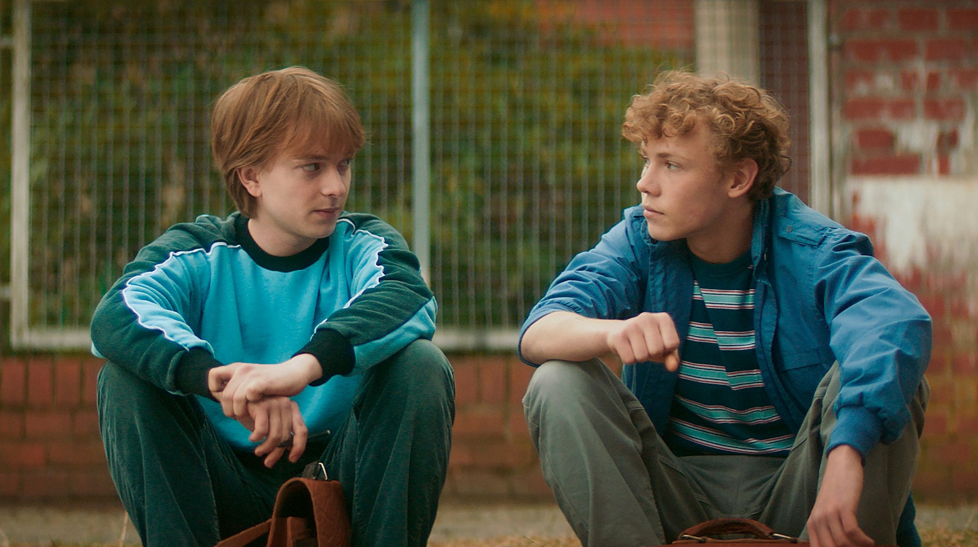 Maik Balthasar und Robert Karow sitzen als Jugendliche nebeneinander vor Maiks Haus und schauen sich an.