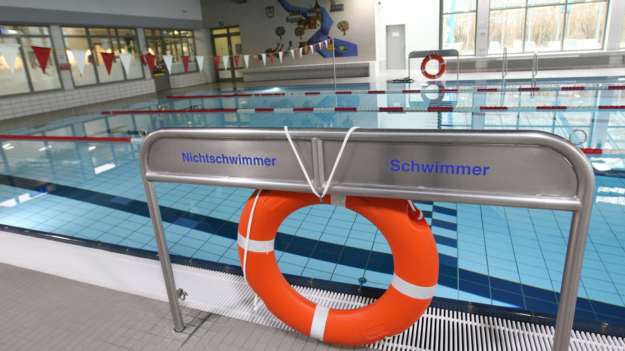 Blick in ein Schwimmbad mit einem Rettungsring und Schildern für die Bereiche für Schwimmer und Nichtschwimmeram Beckenrand.