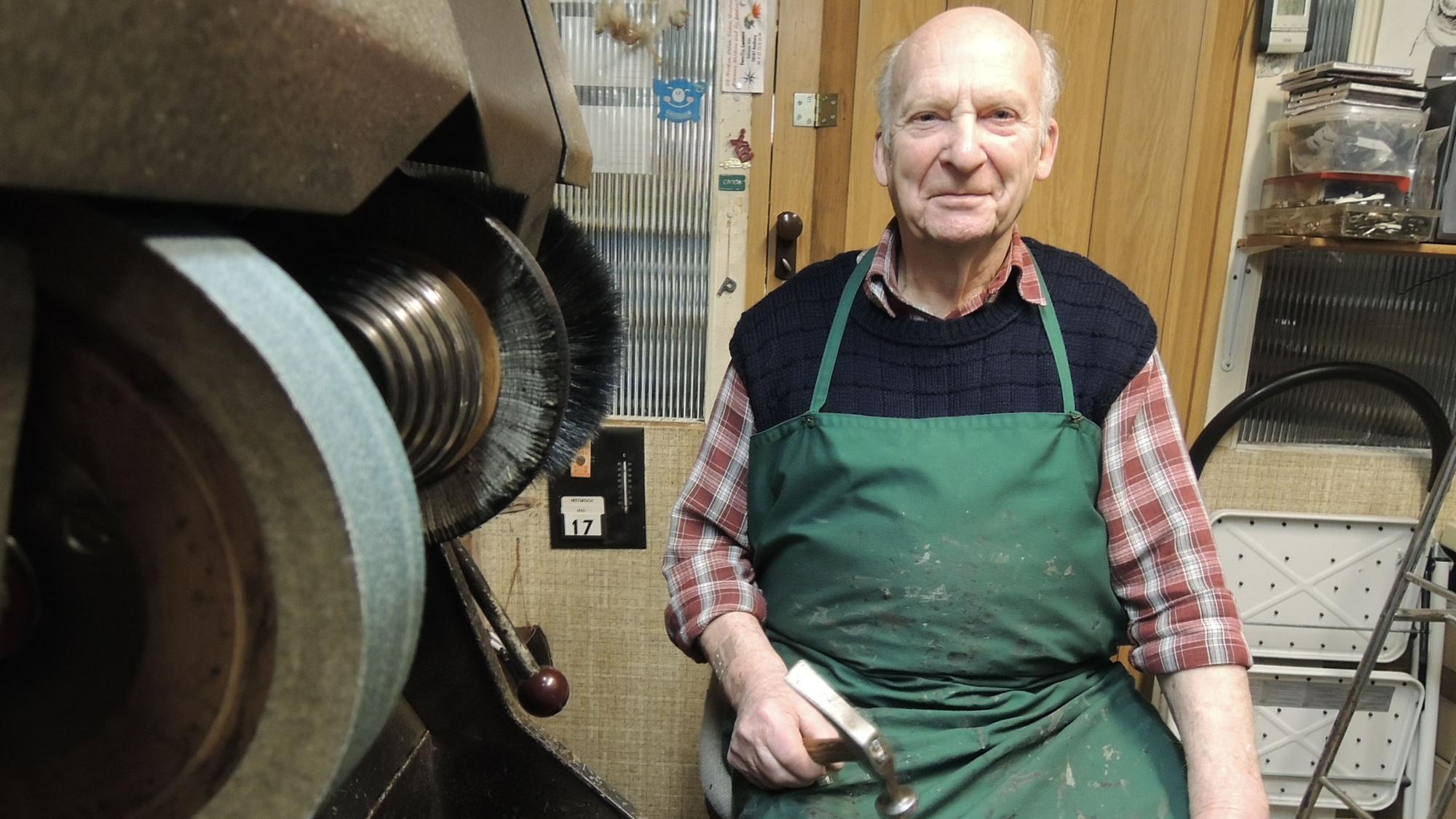 Hubert Glatzen sitzt in am Arbeitsplatz in seinem Schuhmachergeschäft in Bedburg.
