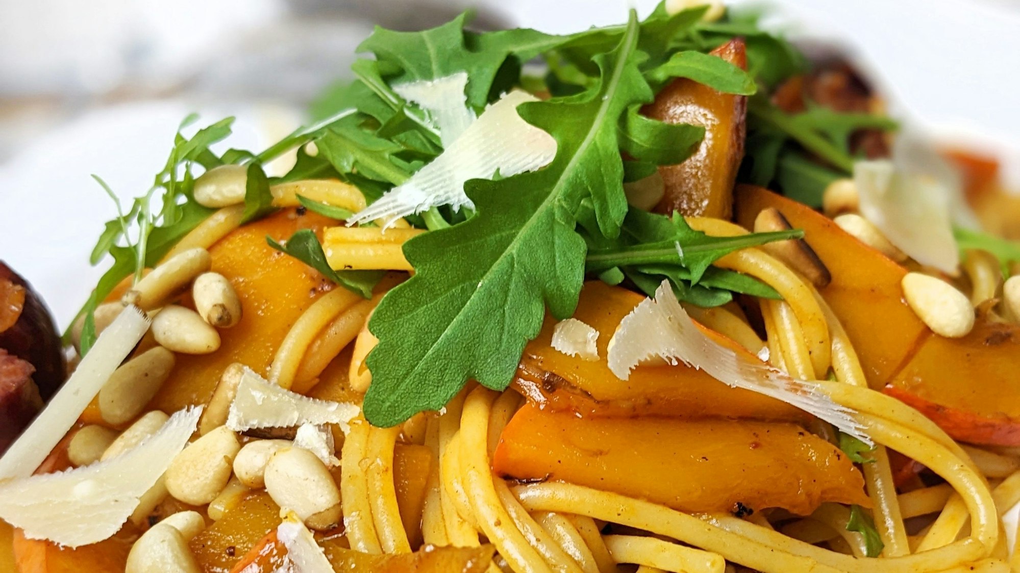 Pasta mit Kürbis, garniert mit Pinienkernen, Parmesan und Rucola.