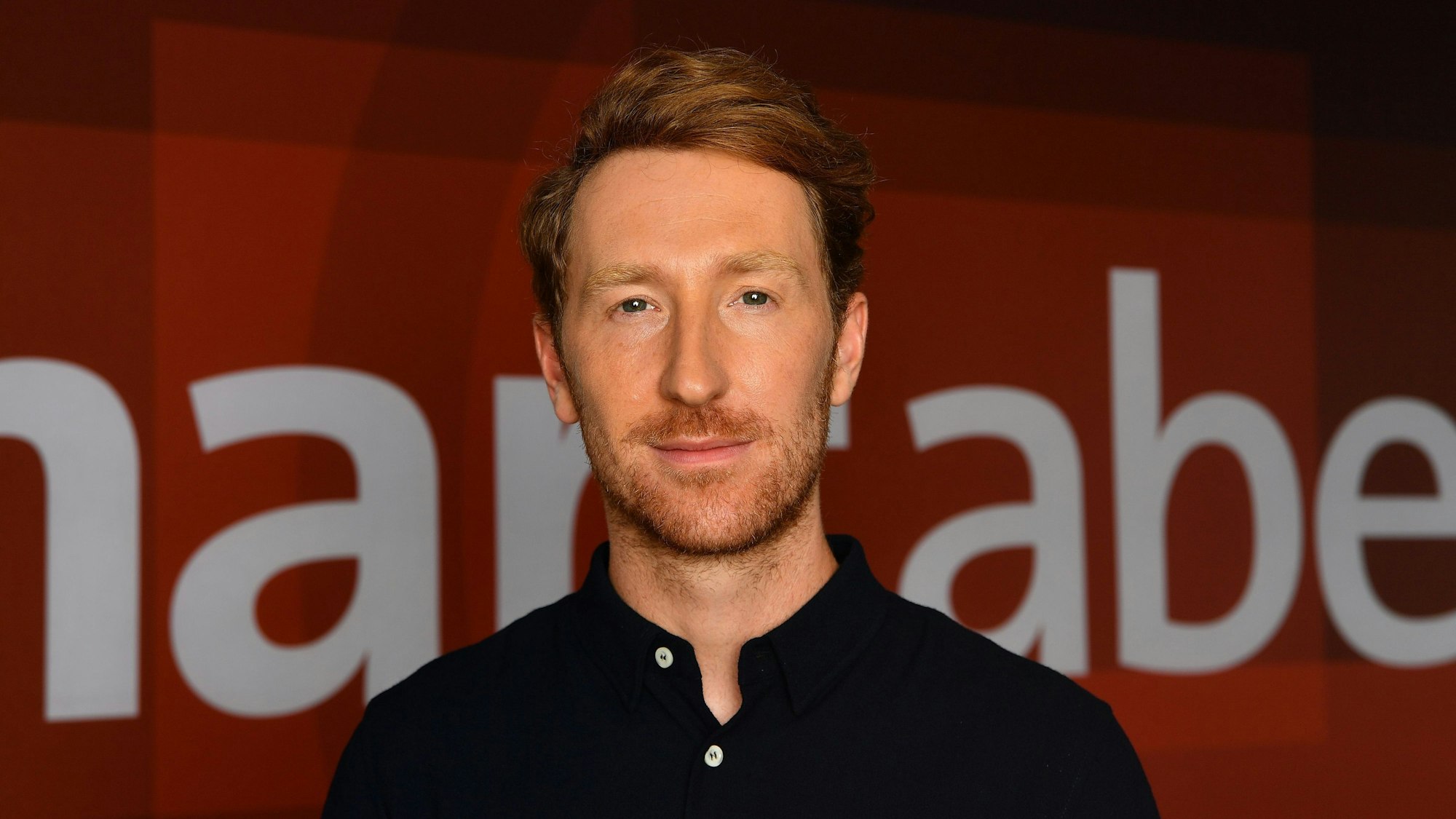 Louis Klamroth auf einem roten Teppich und schaut in die Kamera. Hinter ihm ist die Aufschrift „hart aber fair“