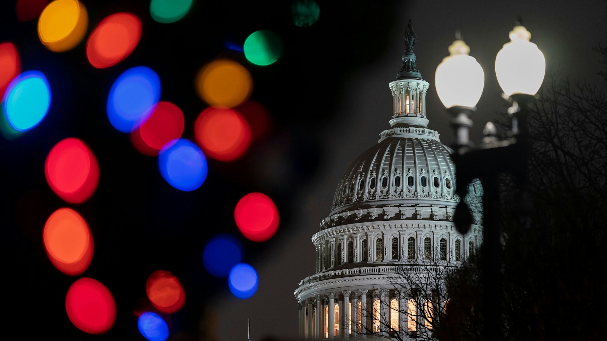 Zu sehen ist die Kuppel des Kapitols bei Nacht angestrahlt. Im Vordergrund sind unscharf Laternen und Lichtpunkte zu erkennen.