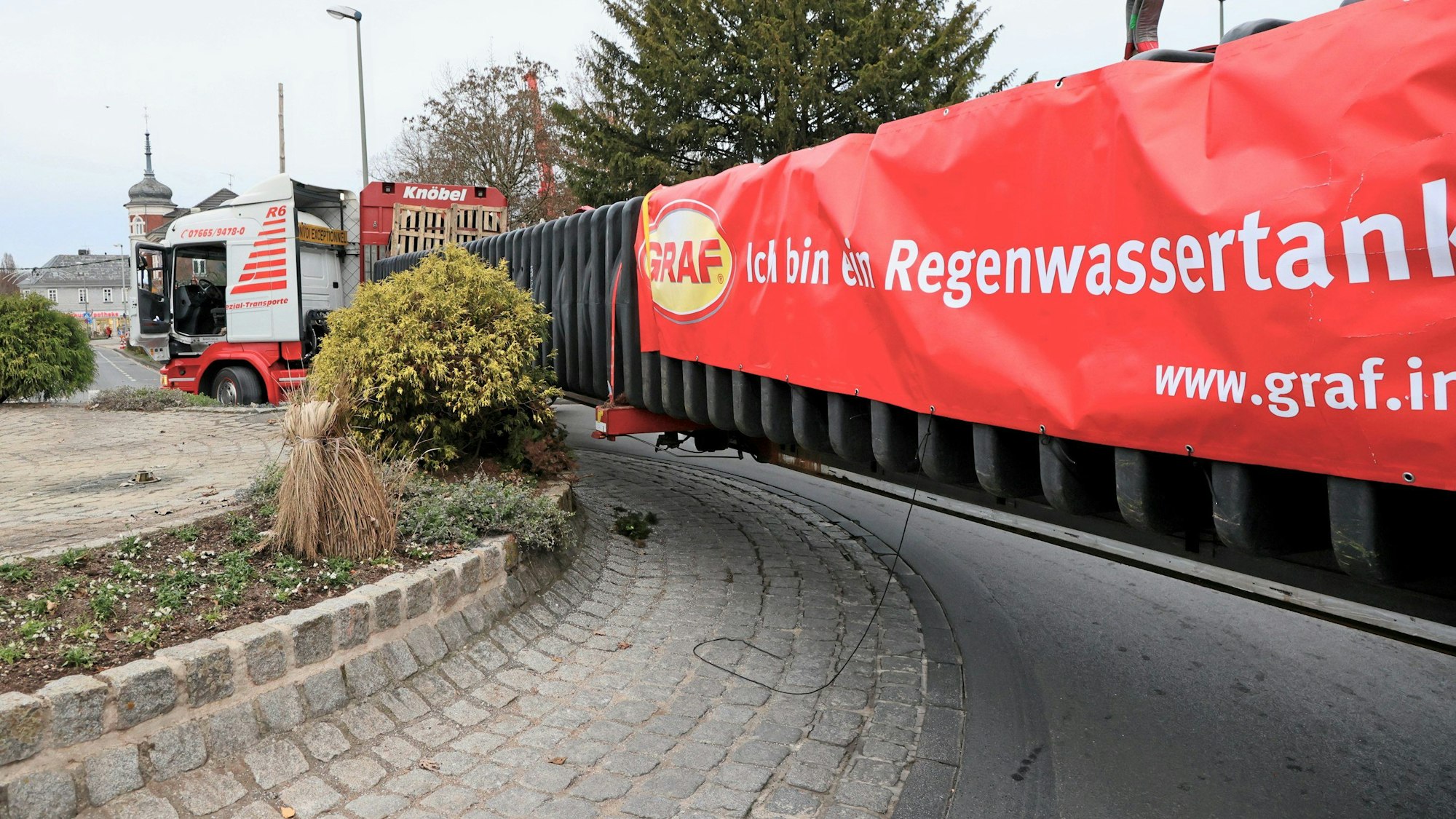 Der überlange Schwertransport schrammt am Brunnen-Kreisverkehr an der Mauer entlang und steckt fest.
