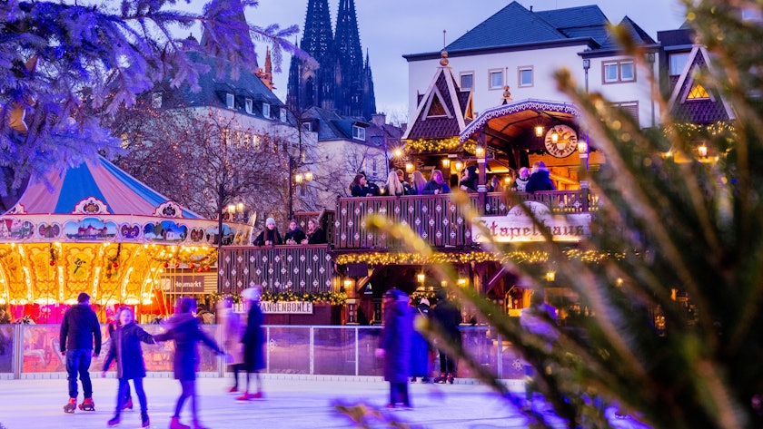 Besucher fahren auf einer Eisbahn auf dem Weihnachtsmarkt auf dem Heumarkt Schlittschuh.