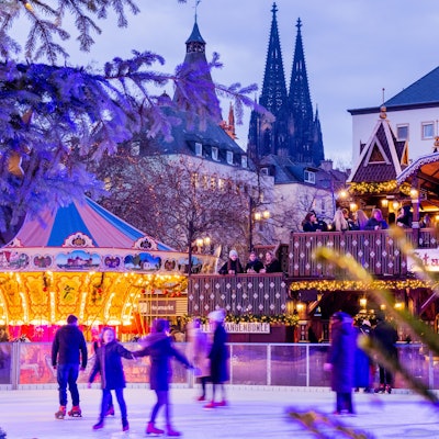Besucher fahren auf einer Eisbahn auf dem Weihnachtsmarkt auf dem Heumarkt Schlittschuh.