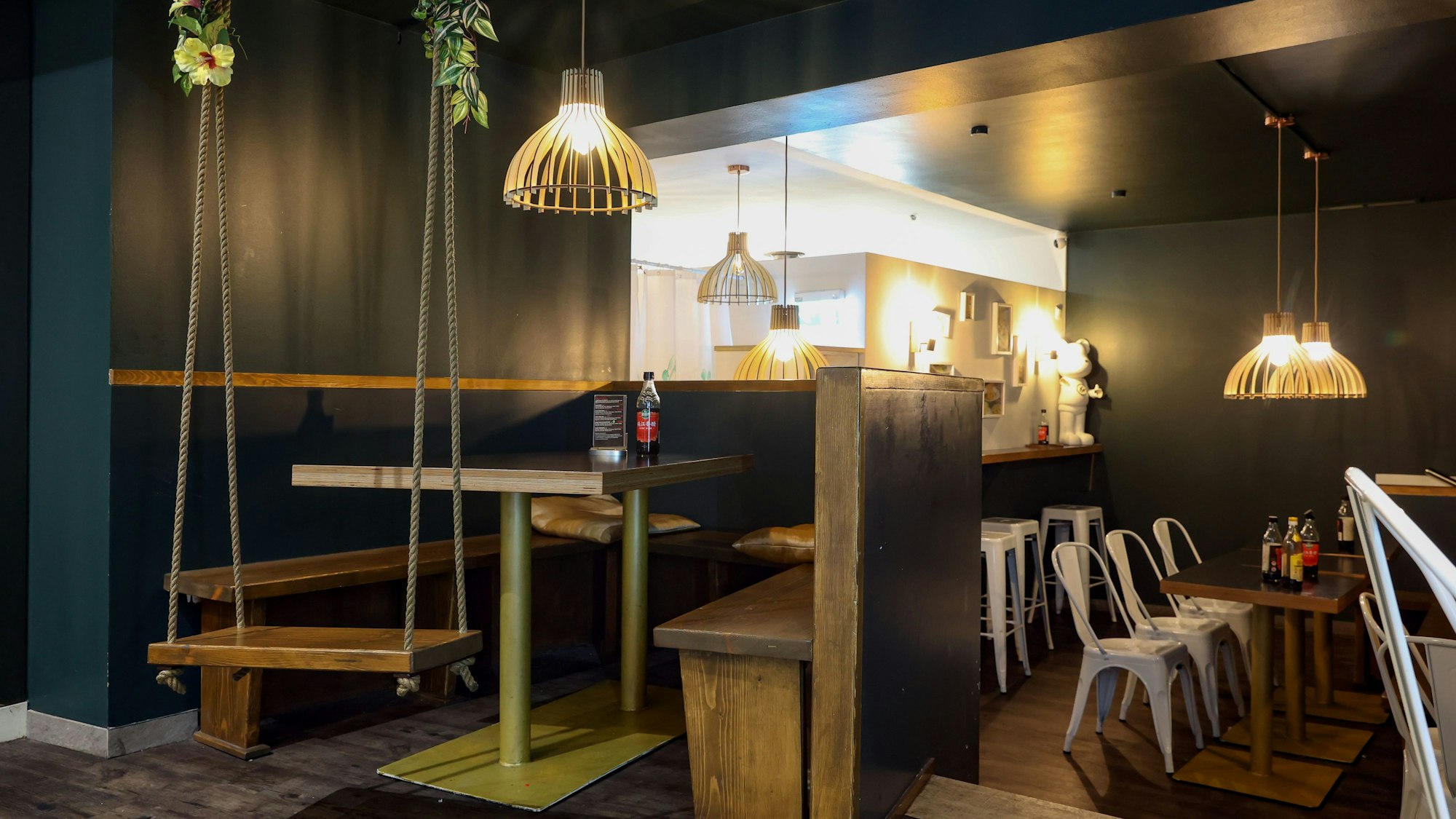 Holztische in einem Restaurant, links im Vordergrund hängt eine Schaukel von der Decke