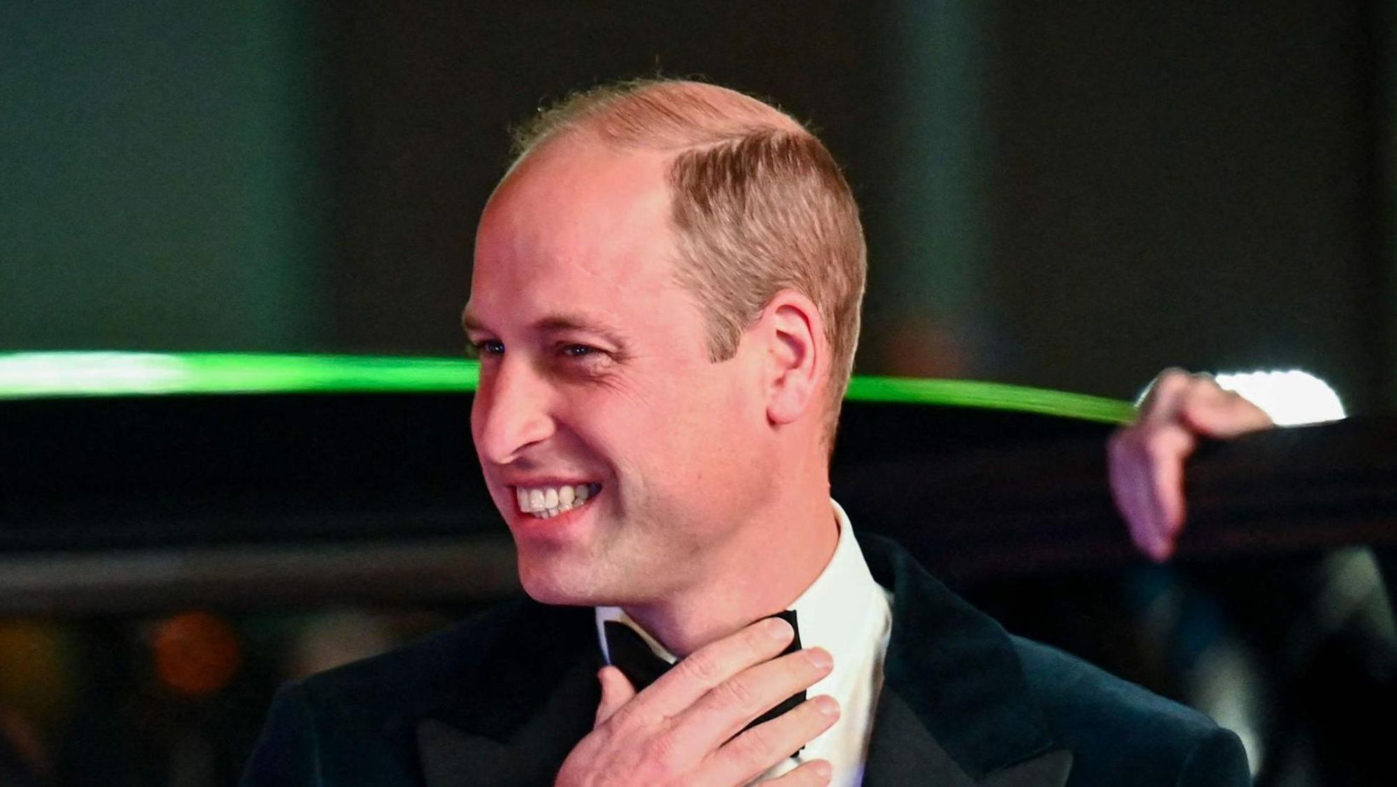 Prinz William mit Fliege und Anzug. Er grinst und steigt aus einem Auto.
