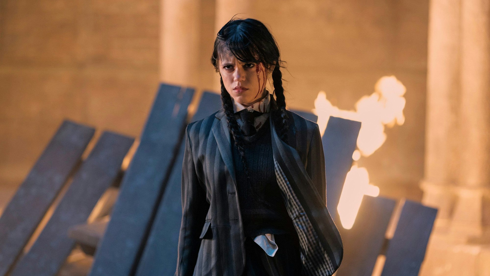 Jenna Ortega steht in einer Serienszene vor einem brennenden Bretterhaufen.