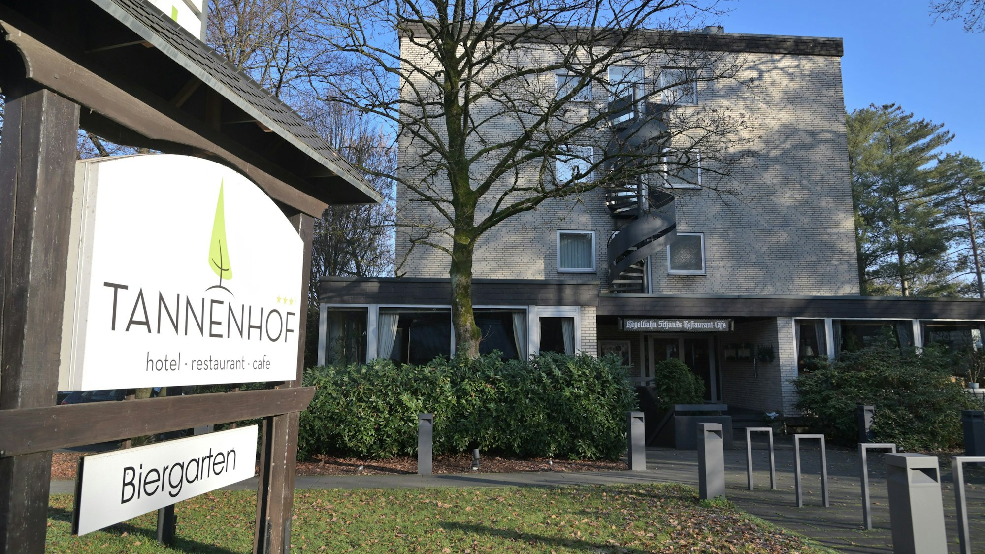 Im Vordergrund steht ein Schild mit der Aufschrift „Tannenhof. Hotel - Restaurant-Café“ sowie „Biergarten“, im Hintergrund ist das Hotelgebäude zu sehen.
