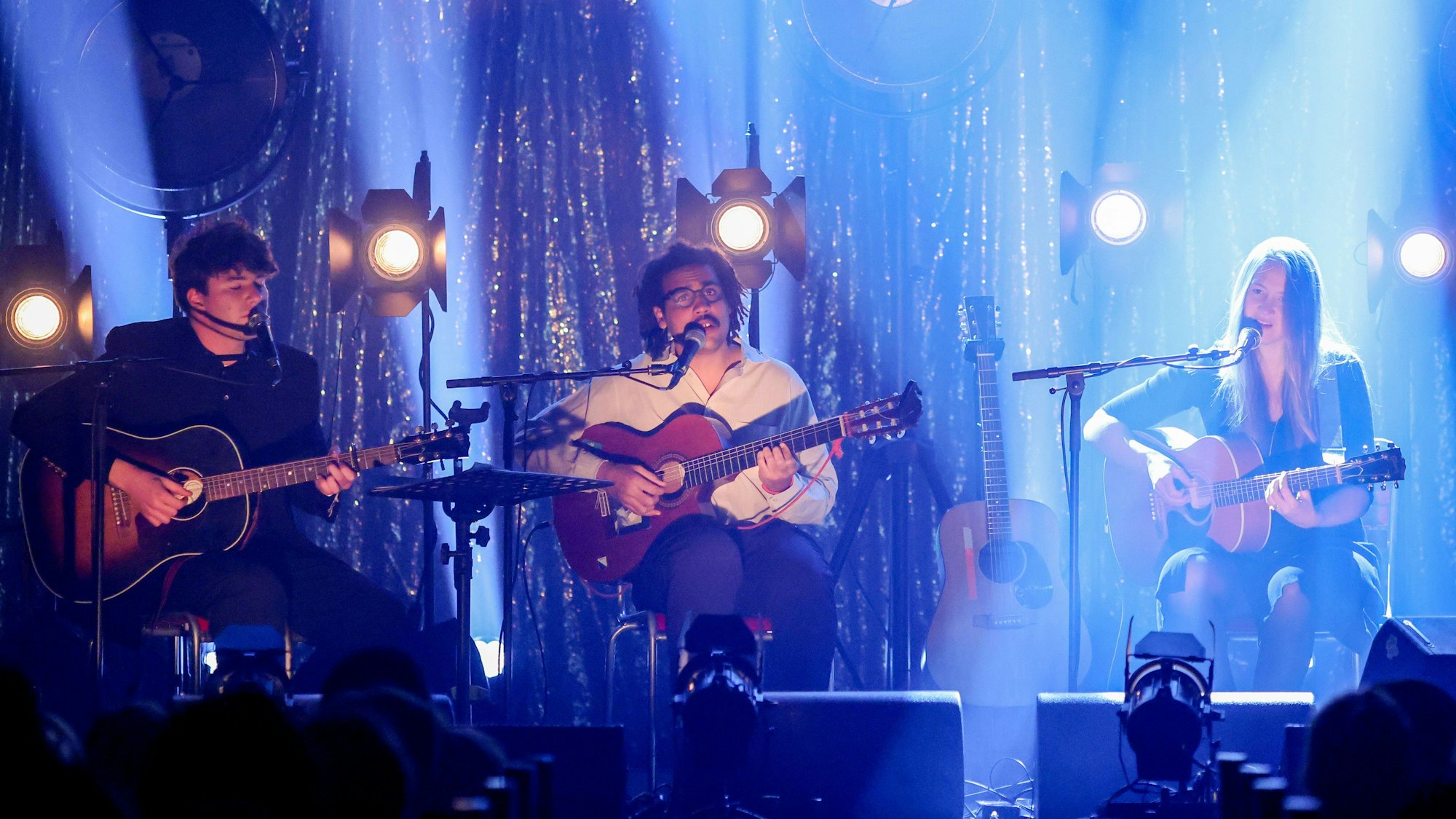 Faber (v.l.), Dino Brandão und Sophie Hunger sitzen in der Kulturkirche in Nippes, angestrahlt von Scheinwerfern.