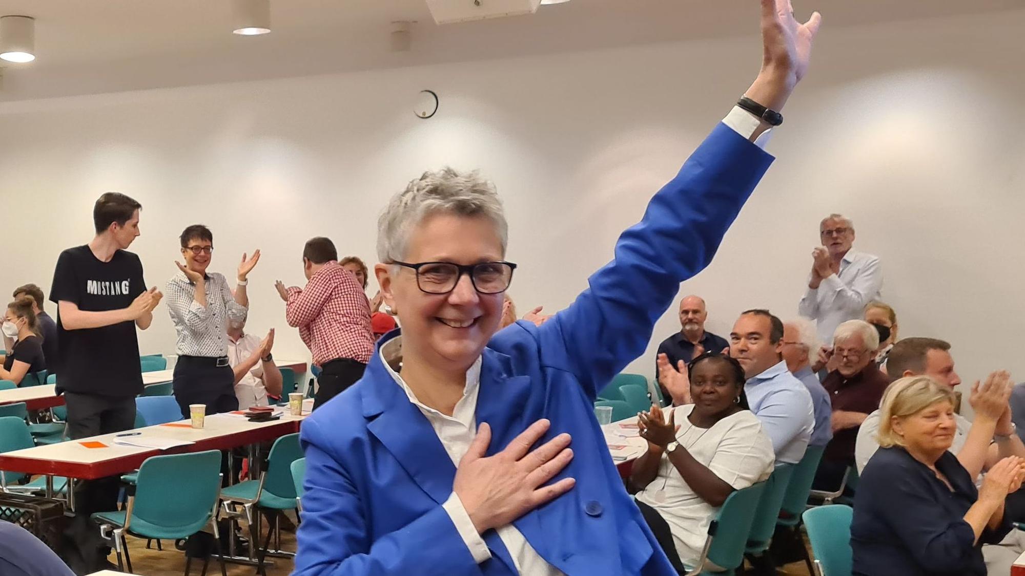 Heike Steinhäuser winkt nach ihrer Wahl zu SPD-Vorsitzenden im Kreis ihren Genossen zu. Die Frau mit dem grauen Kurzhaarschnitt trägt ein blaues Sacko und eine schwarze Hose.