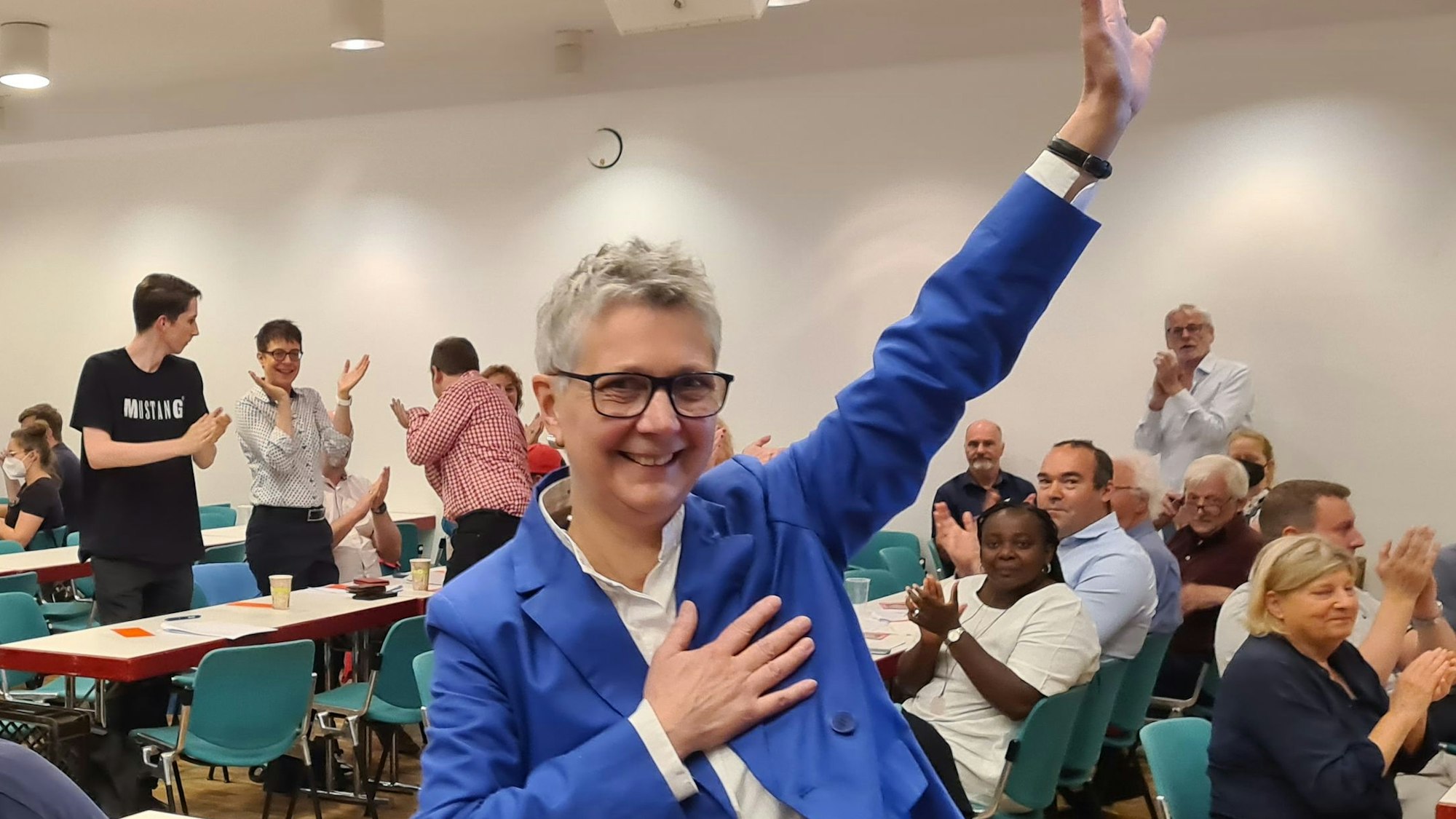 Heike Steinhäuser winkt nach ihrer Wahl zu SPD-Vorsitzenden im Kreis ihren Genossen zu. Die Frau mit dem grauen Kurzhaarschnitt trägt ein blaues Sacko und eine schwarze Hose.
