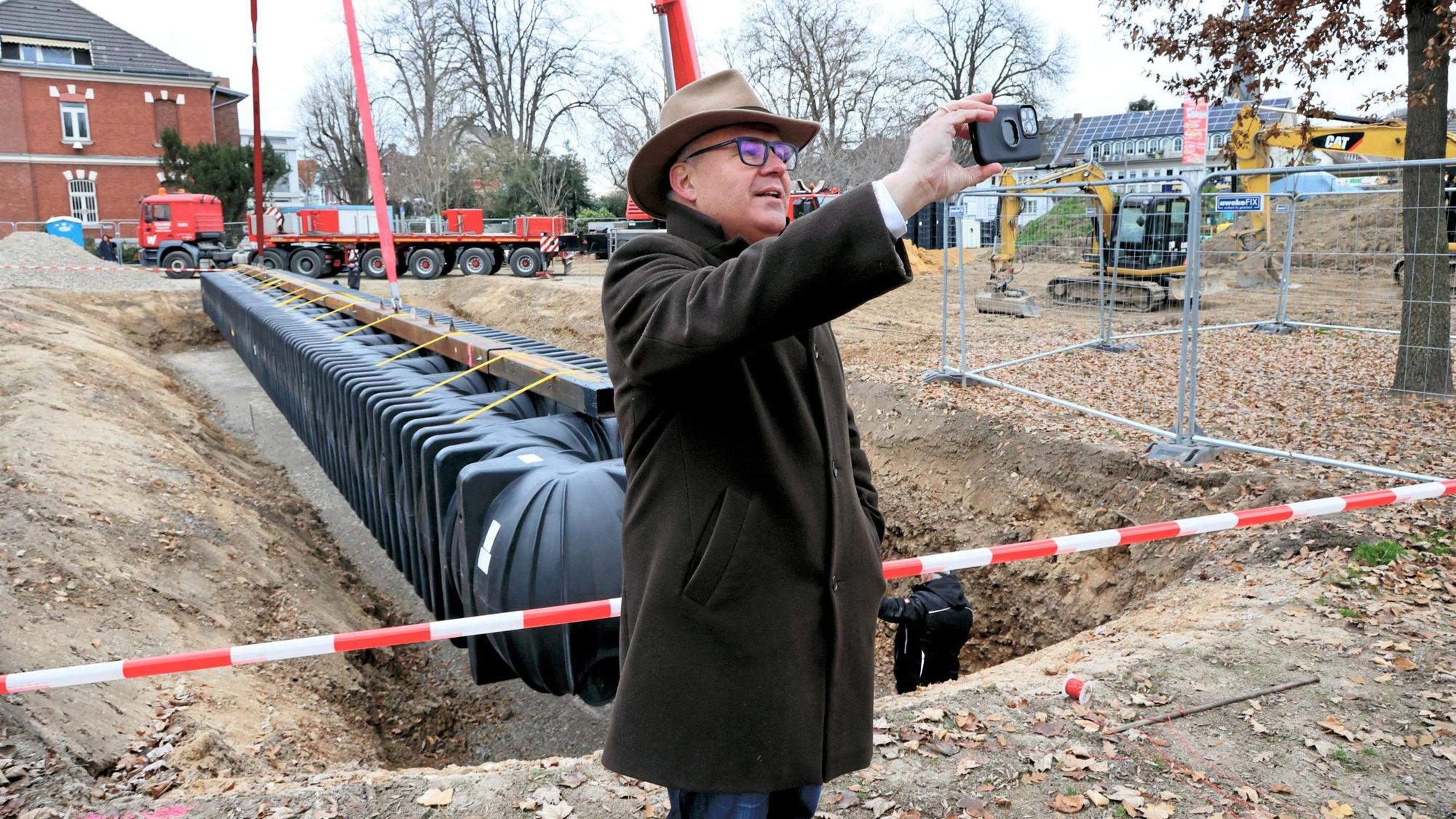 Bürgermeister Frank Steffes steht auf der Baustelle und macht mit seinem Handy ein Selfie-Foto, als der Tank direkt neben ihm in die Baugrube einschwebt.