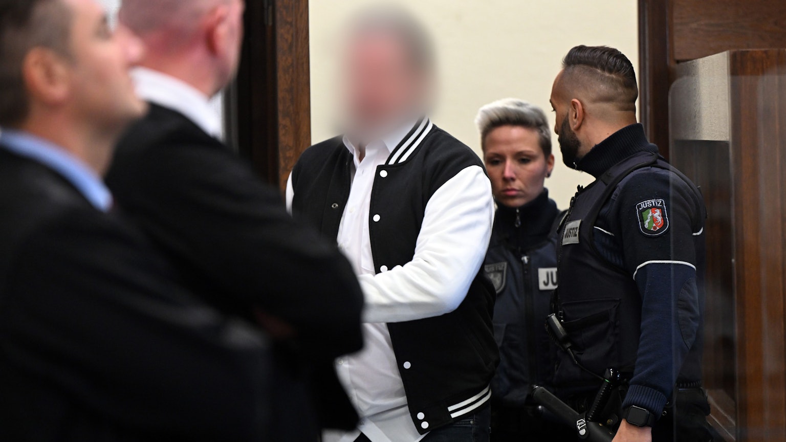 Der Angeklagte (m) wird von mehreren Justizbeamten in den Gerichtssaal geführt.