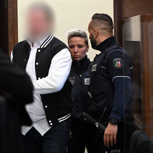 Der Angeklagte (m) wird von mehreren Justizbeamten in den Gerichtssaal geführt.