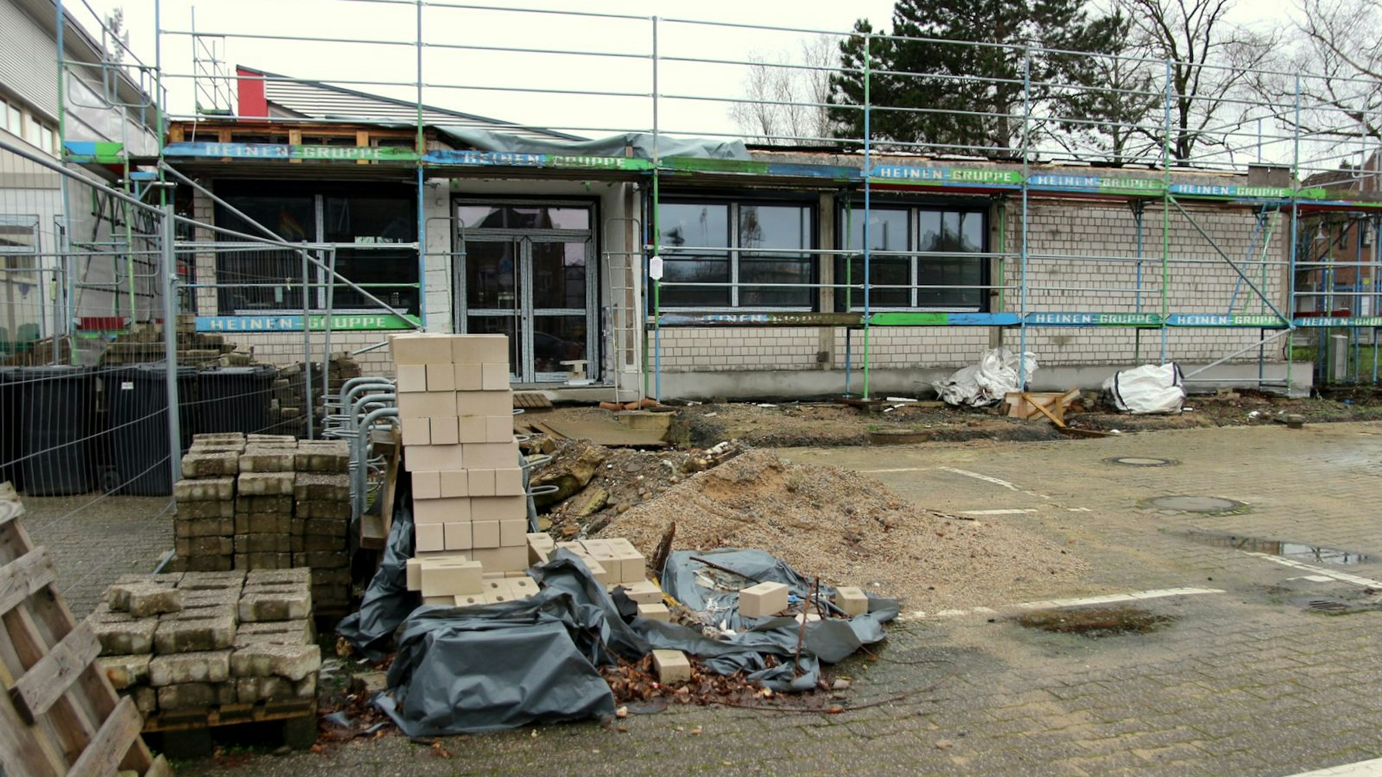 Auf dem Foto ist ein Erweiterungsbau der Horionschule in Pulheim zu sehen. Das Gebäude ist eingerüstet, davor liegt Baumaterial wie Steine und Sand.