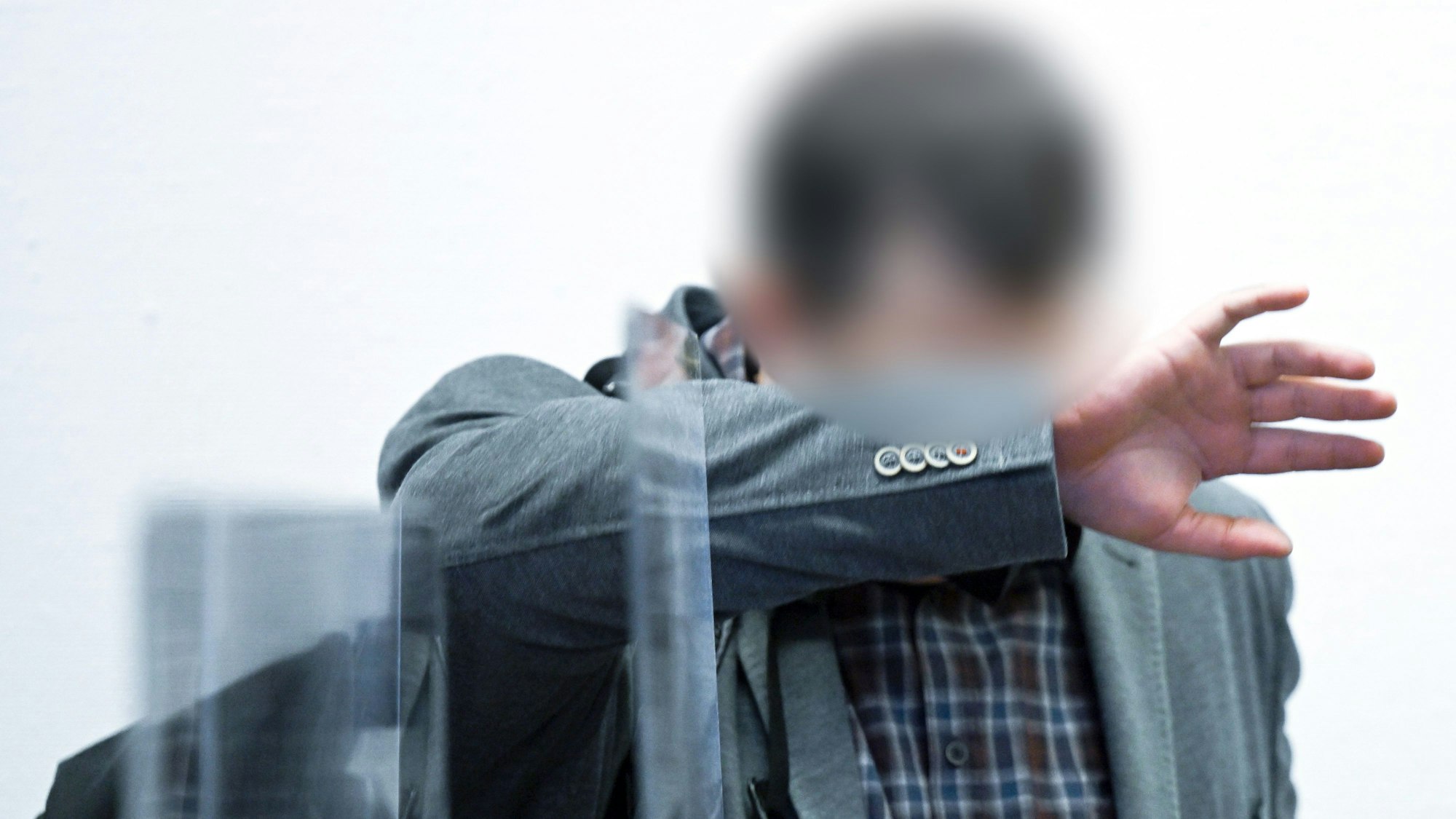 Der Angeklagte steht vor dem Beginn des Prozesses im Gerichtssaal im Landgericht und bedeckt sein Gesicht.