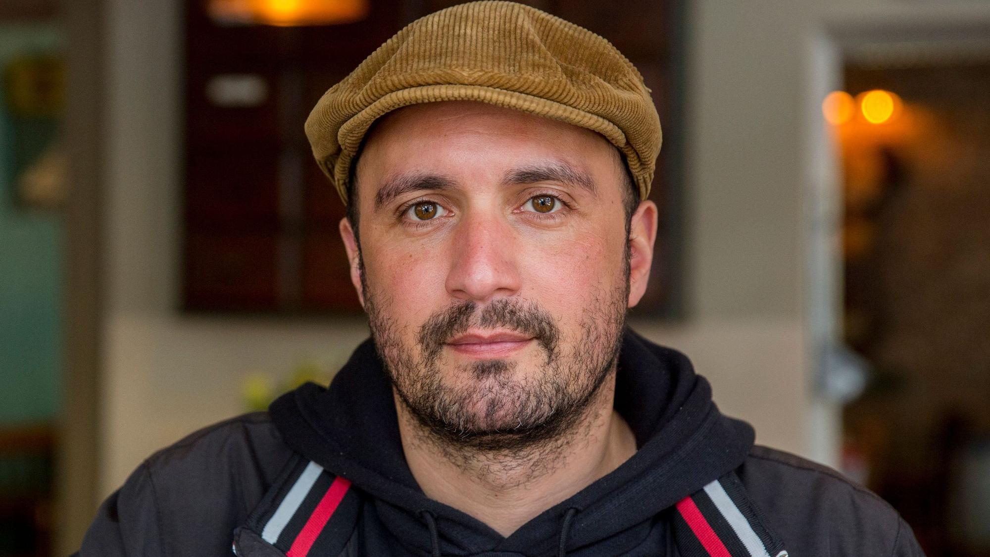 Porträt vom Kölner Gastronom Daniel Rabe, im Kapuzenpullover und mit gelber Schiebermütze.