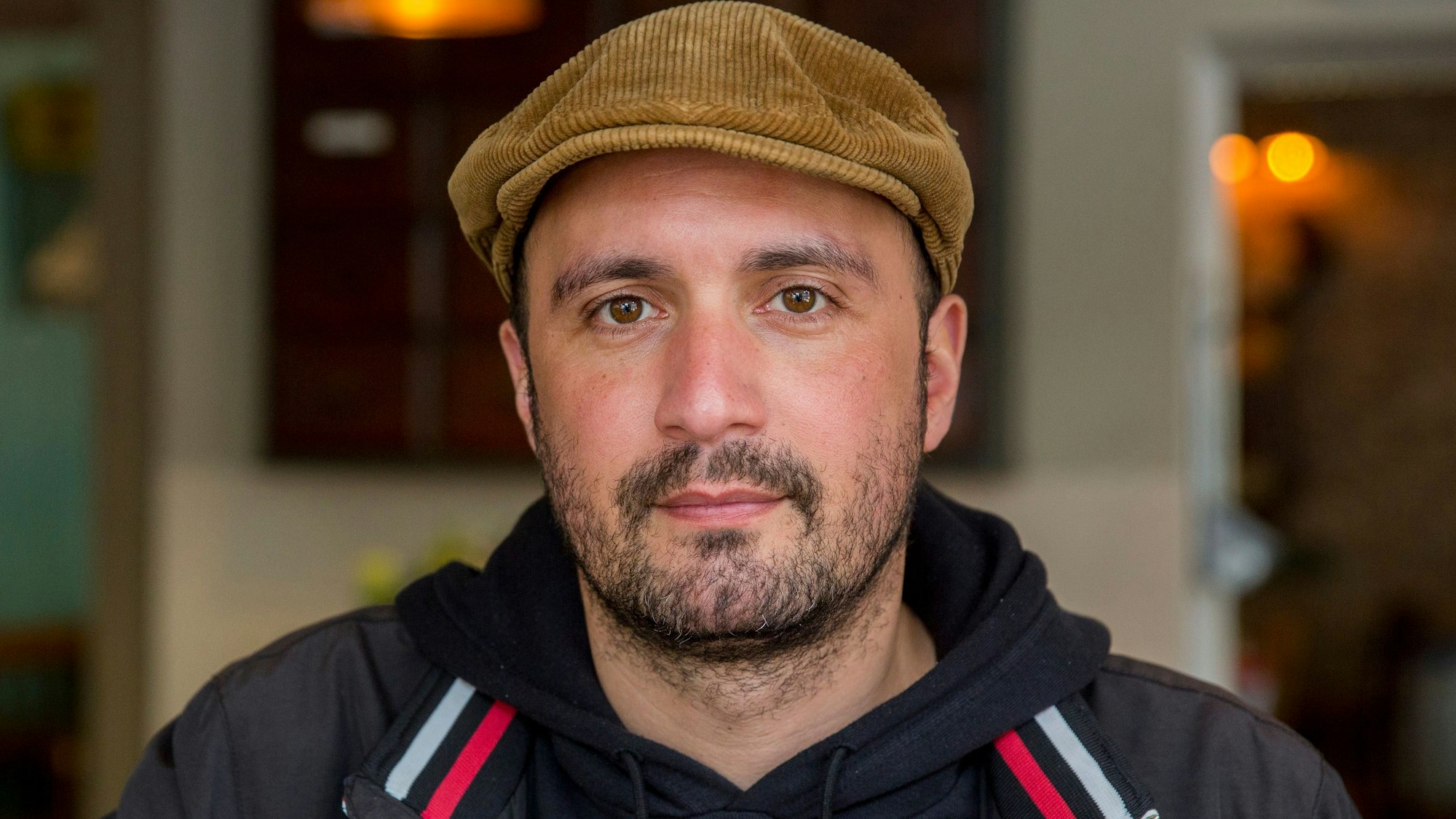Porträt vom Kölner Gastronom Daniel Rabe, im Kapuzenpullover und mit gelber Schiebermütze.