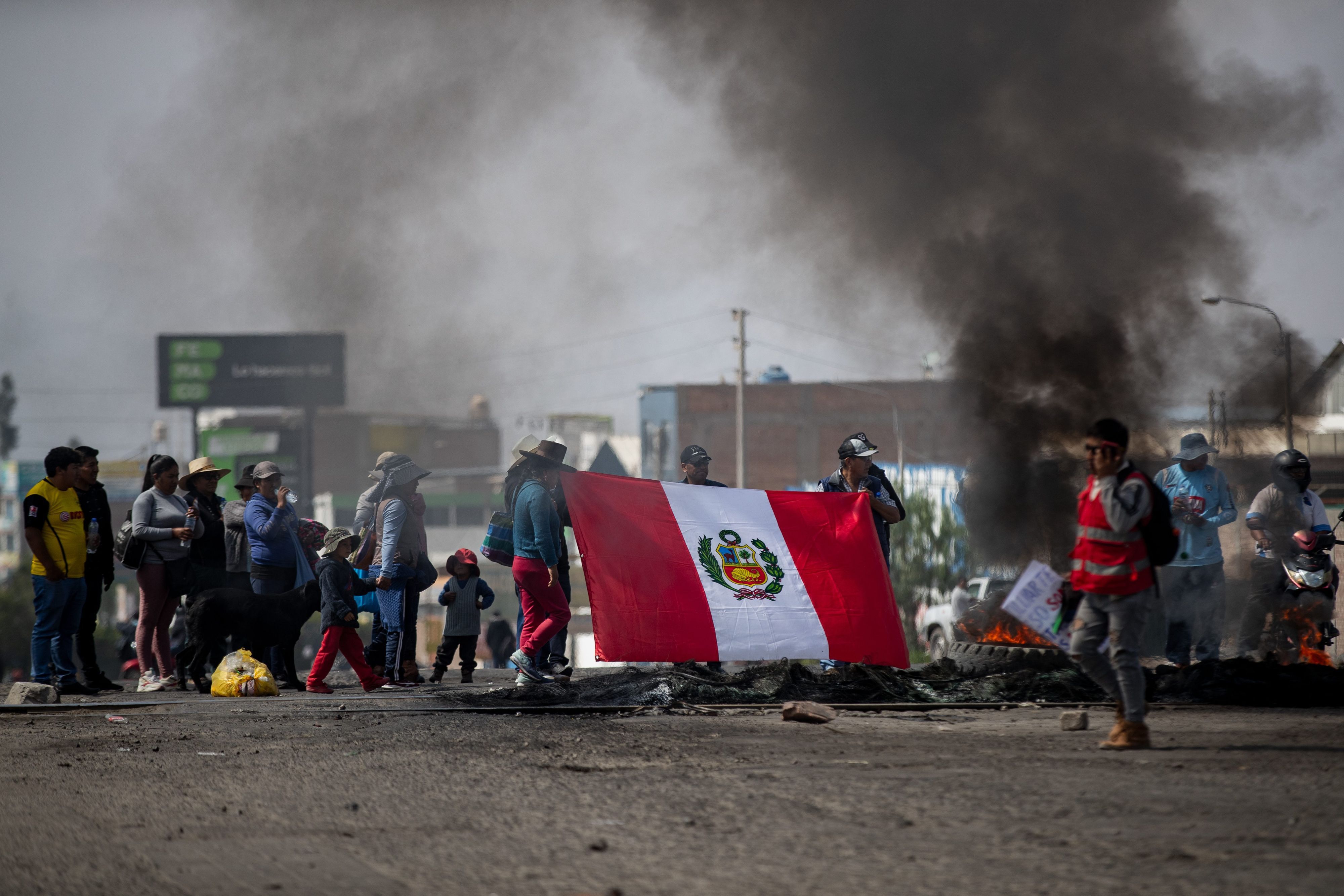 Demonstranten protestierenauf einer Straße neben brennenden Reifen und halten eine peruanische Flagge hoch.