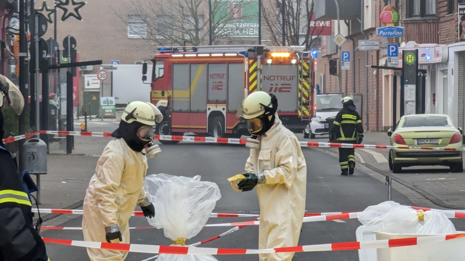 Feuerwehrleute in Sicherheitsanzügen und mit Atemschutzmasken sichern in Plastiksäcken Material aus der Arztpraxis.