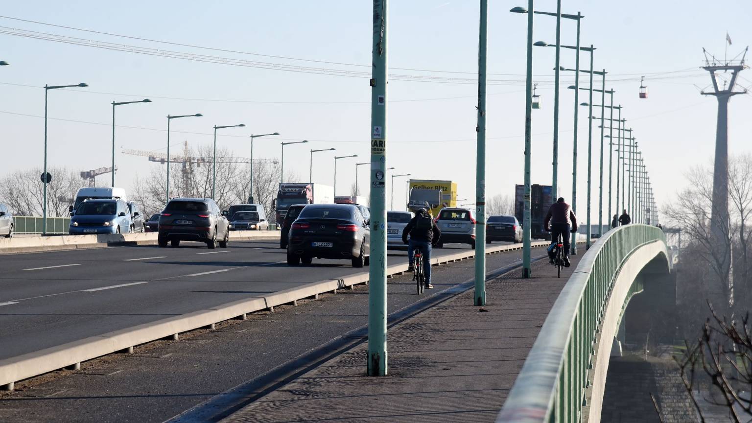 Viel Verkehr auf der Kölner Zoobrücke. Neben Autos und Lkws fahren Radfahrer. Viele Laternenmasten stehen am Straßenrand.