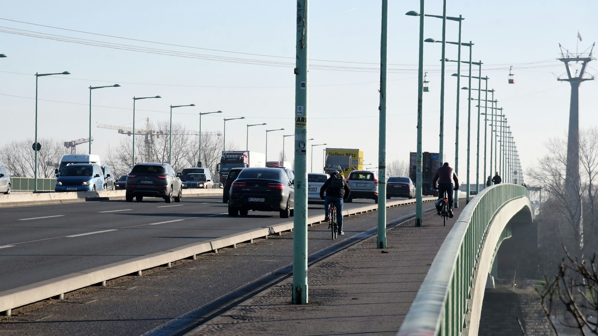Viel Verkehr auf der Kölner Zoobrücke. Neben Autos und Lkws fahren Radfahrer. Viele Laternenmasten stehen am Straßenrand.