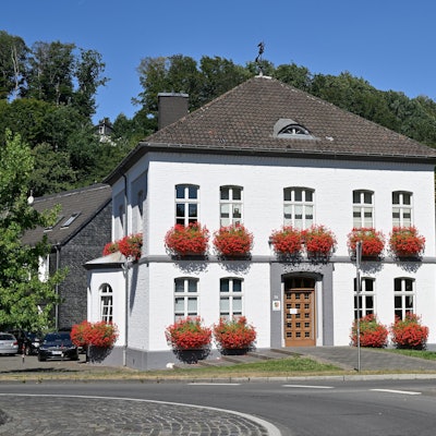 Am Odenthaler Rathaus hängen Blumenkästen. Im Hintergrund stehen Bäume.