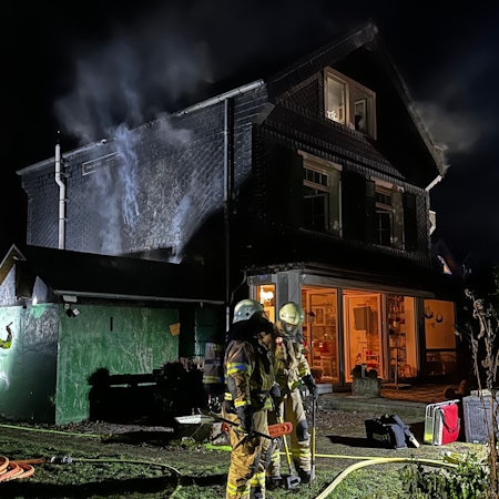 Feuerwehrleute und Polizei an dem noch rauchenden Brandhaus in Bergisch Gladbach-Schildgen.