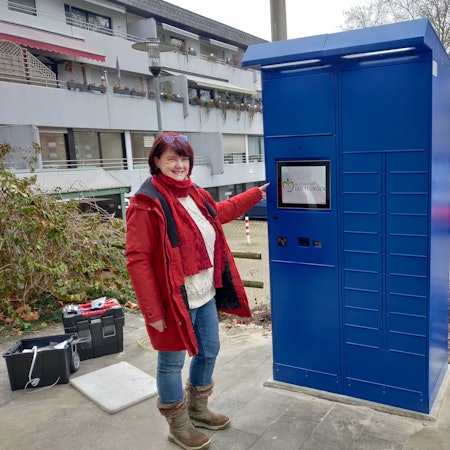 Amtsleiterin Brigitte Gutendorf steht neben dem blauen Ausweis-Automaten vor dem Rathaus.