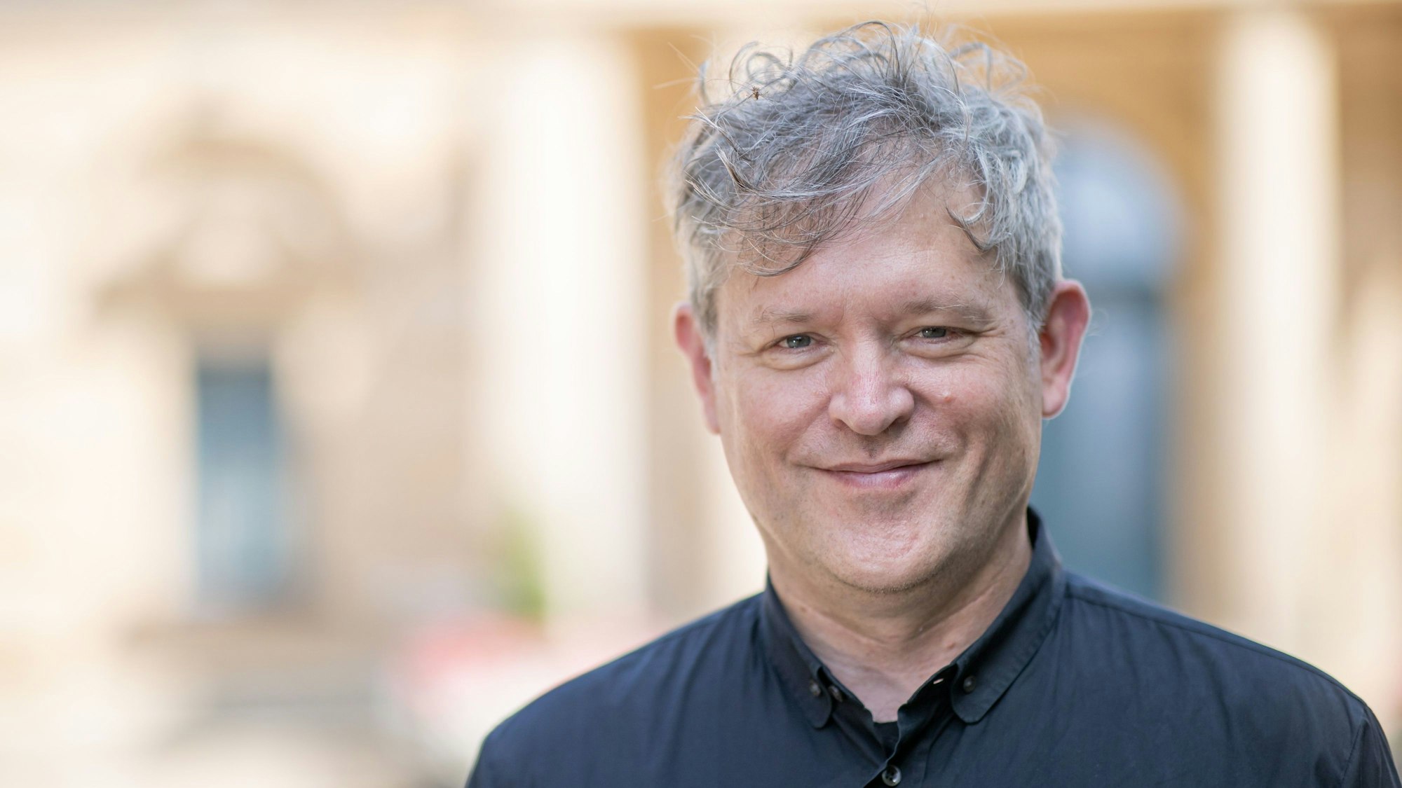 Der US-amerikanische Regisseur Jay Scheib steht vor dem Festspielhaus. Er hat ein schwarzes Hemd an.