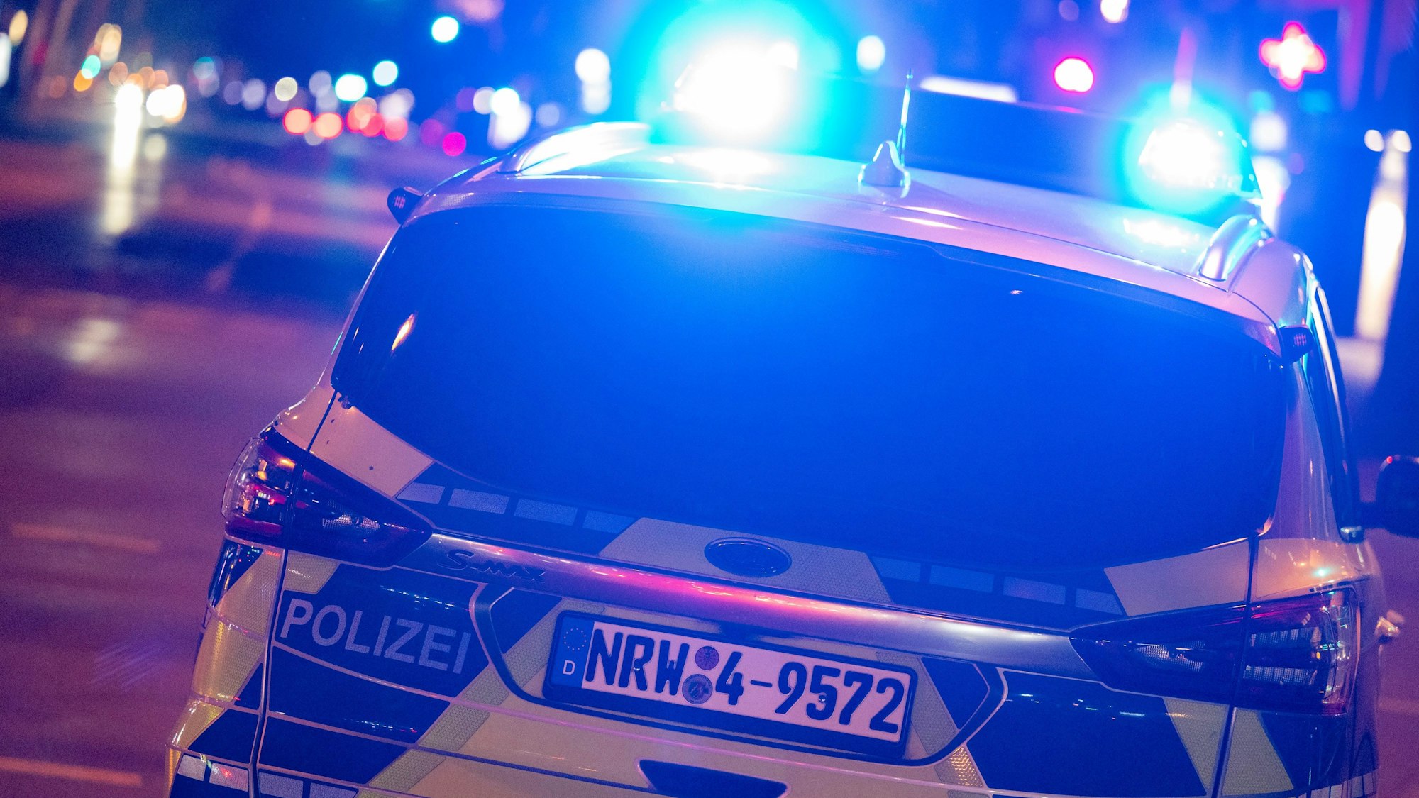 Ein Polizeiwagen fährt nachts mit Blaulicht über eine Straße.