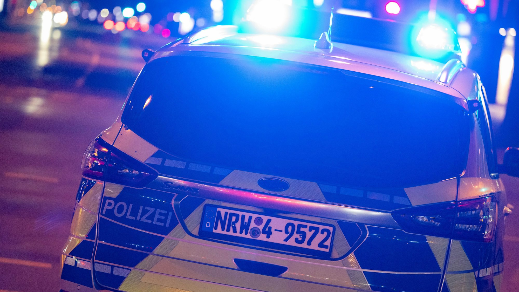 Ein Einsatzfahrzeug der Kölner Polizei von hinten mit Blaulicht bei Nacht.