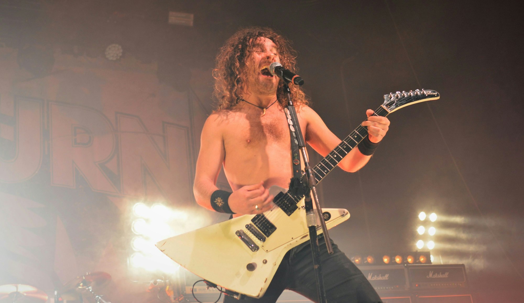 Joel O'Keeffe oberkörperfrei mit seiner E-Gitarre am Mikrofon.