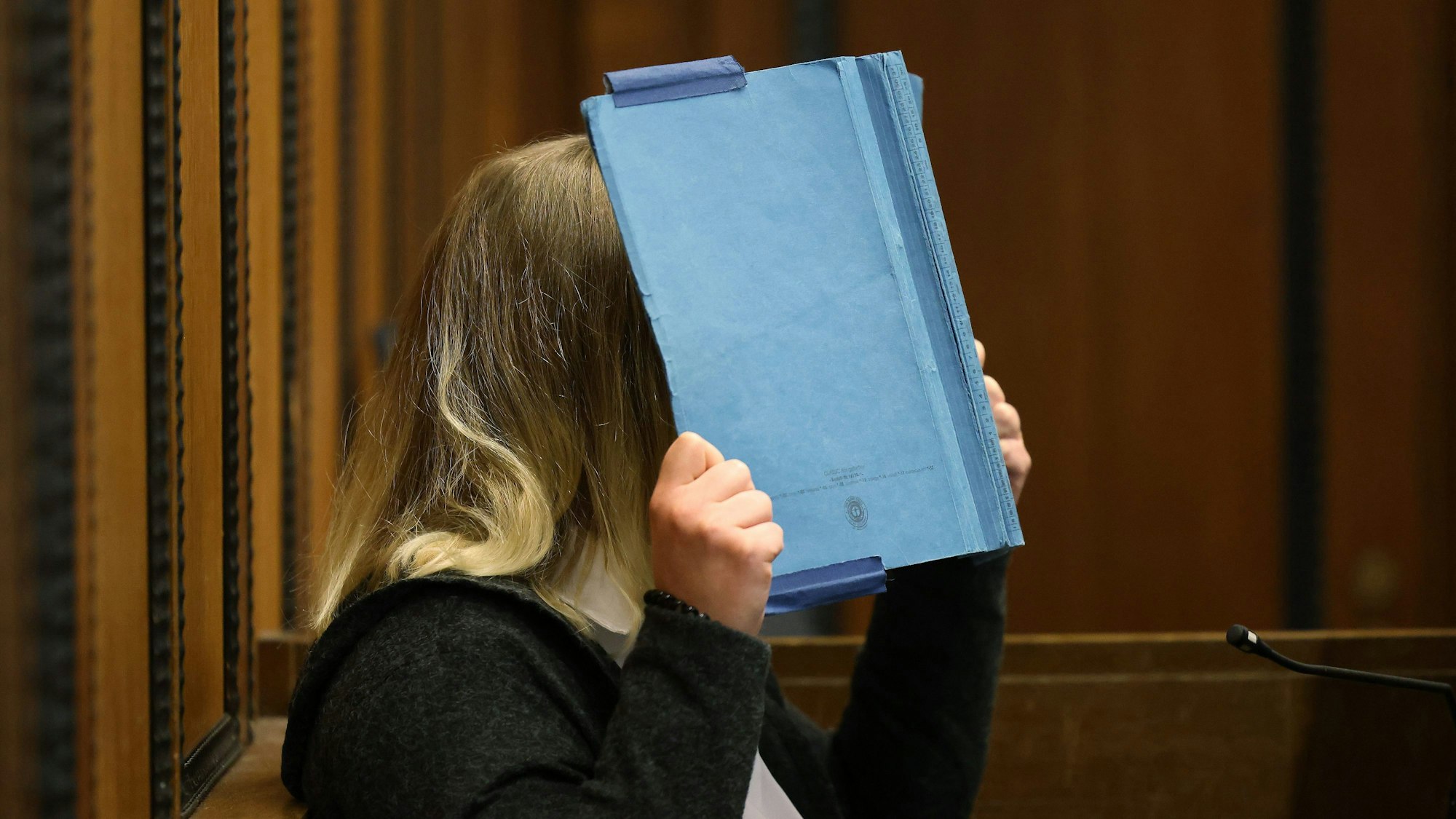 Die Angeklagte deckt beim Prozess im Landgericht ihr Gesicht mit einem blauen Ordner ab.