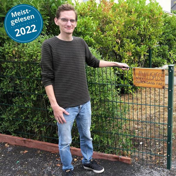 Djordje Atlialp steht vor einem Gartenzaun. Ein Schild daran trägt die Aufschrift „Wikelgasse“.