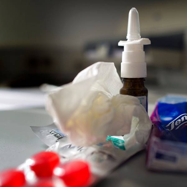 Anti-Erkältungsmittel wie Nasenspray, Halstabletten und Papiertaschentücher liegen auf einem Tisch.