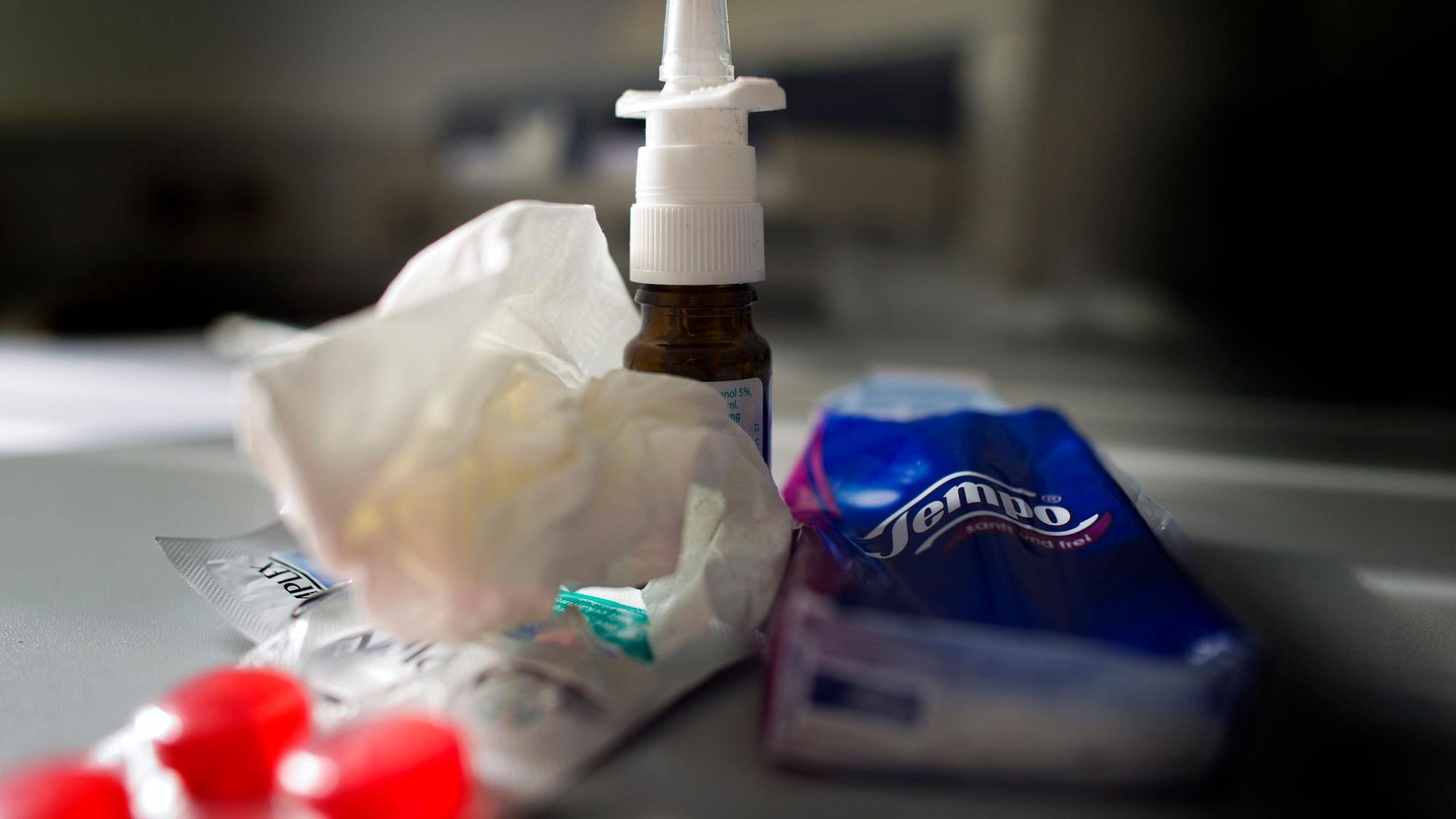 Anti-Erkältungsmittel wie Nasenspray, Halstabletten und Papiertaschentücher liegen auf einem Tisch.