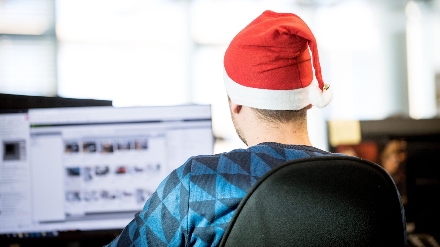 Ein Mann sitzt mit rot-weißer Weihnachtsmütze im Büro an einem Bildschirm.