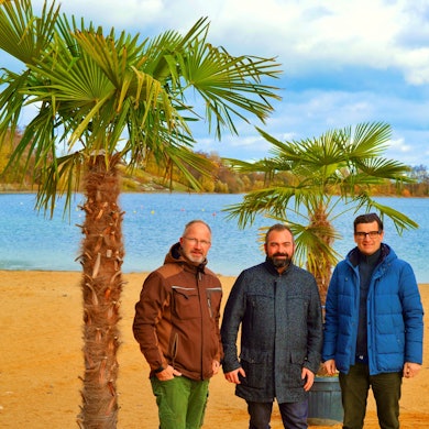 Drei Männer stehen unter Palmen im Seepark Zülpich.