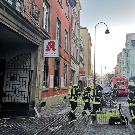 Mehrere Einsatzkräfte der Feuerwehr stehen vor der abgebrannten Apotheke in Deutz.