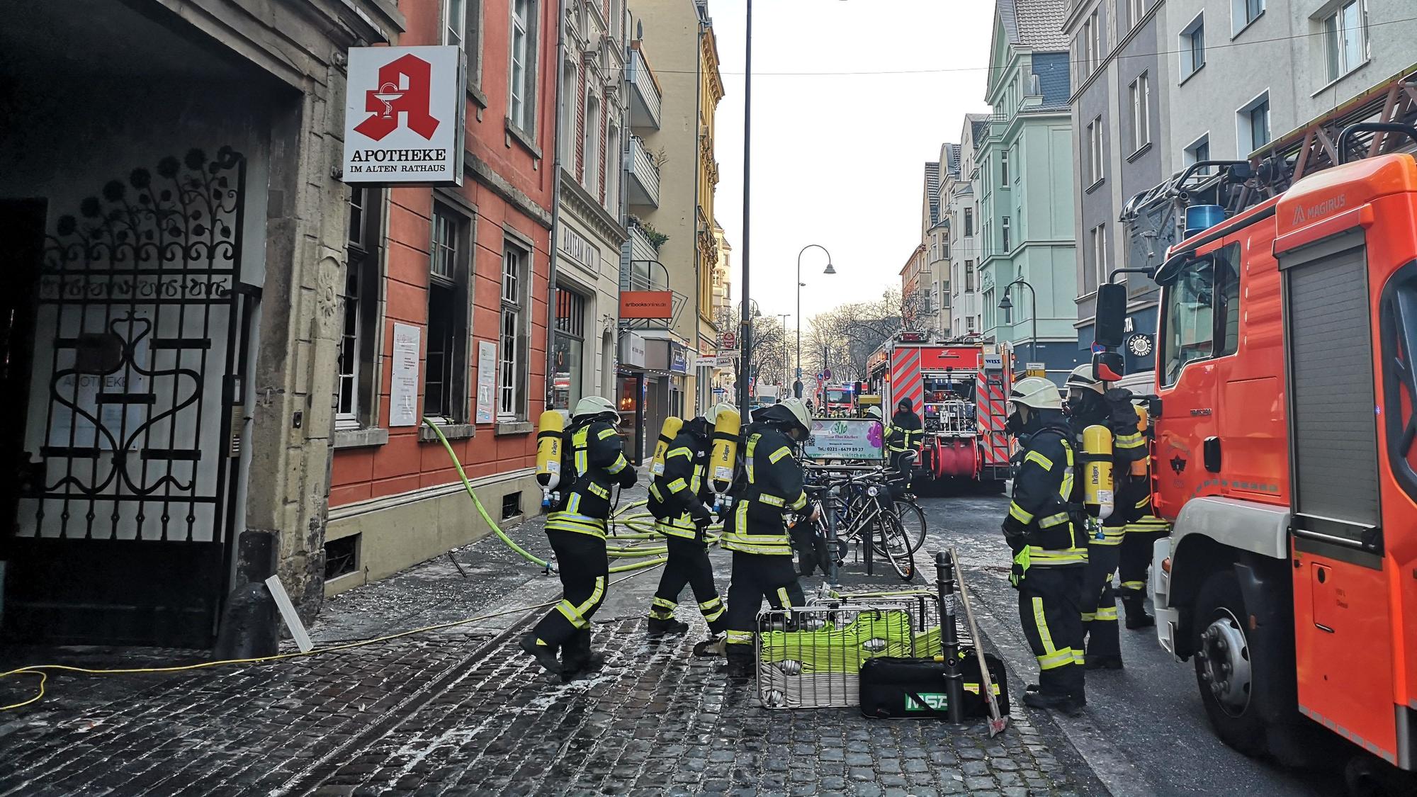 Mehrere Einsatzkräfte der Feuerwehr stehen vor der abgebrannten Apotheke in Deutz.