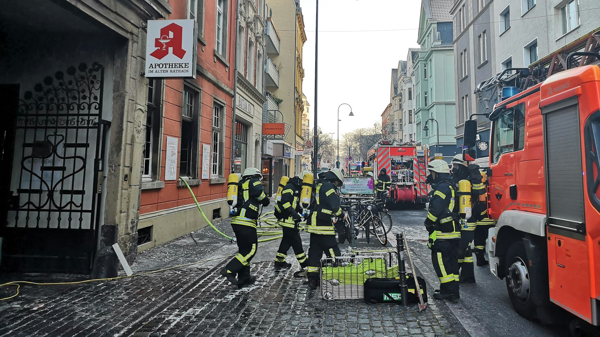 Mehrere Einsatzkräfte der Feuerwehr stehen vor der abgebrannten Apotheke in Deutz.