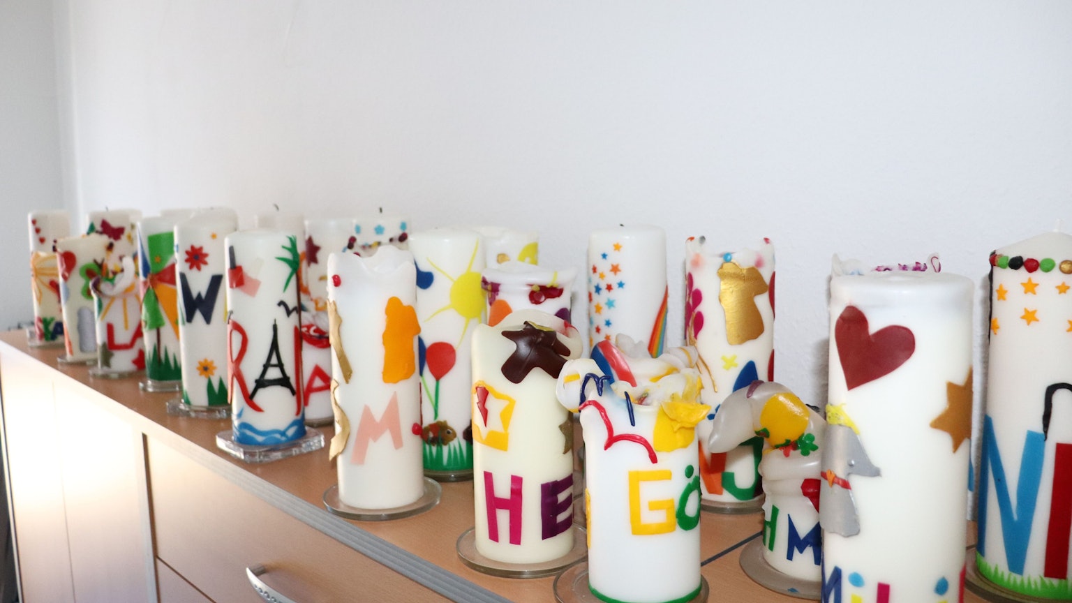 Bunte Kerzen stehen auf einer Ablage, sie erinnern an verstorbene Kinder.