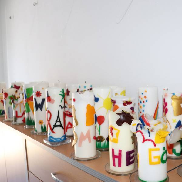 Viele bunte Kerzen mit Kindernamen stehen auf einer Kommode. Sie stehen symbolisch für je ein Kind, das von den ehrenamtlichen Mitarbeitenden des ambulanten Kinder- und Jugendhospizdienstes Köln vor seinem Tod begleitet wurde.