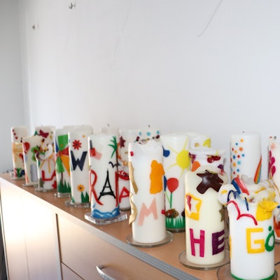 Viele bunte Kerzen mit Kindernamen stehen auf einer Kommode. Sie stehen symbolisch für je ein Kind, das von den ehrenamtlichen Mitarbeitenden des ambulanten Kinder- und Jugendhospizdienstes Köln vor seinem Tod begleitet wurde.